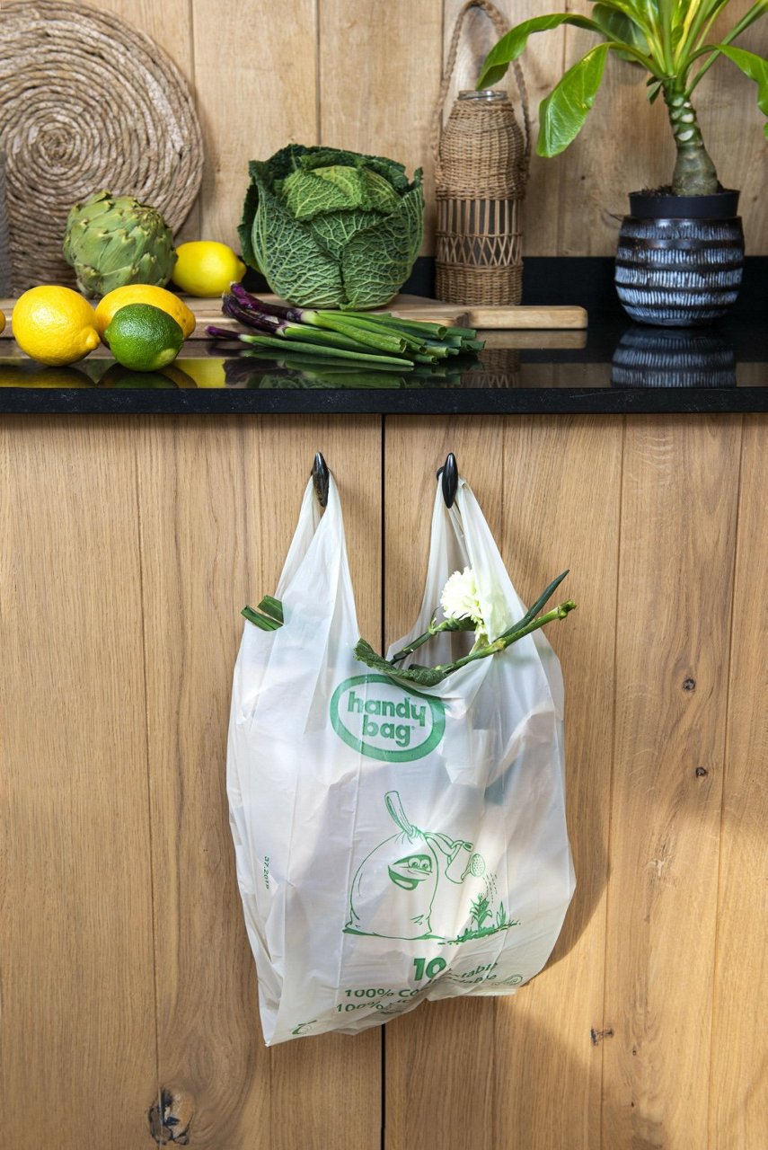 Sac poubelle Handybag compostable à poignées vertes accroché sur un meuble