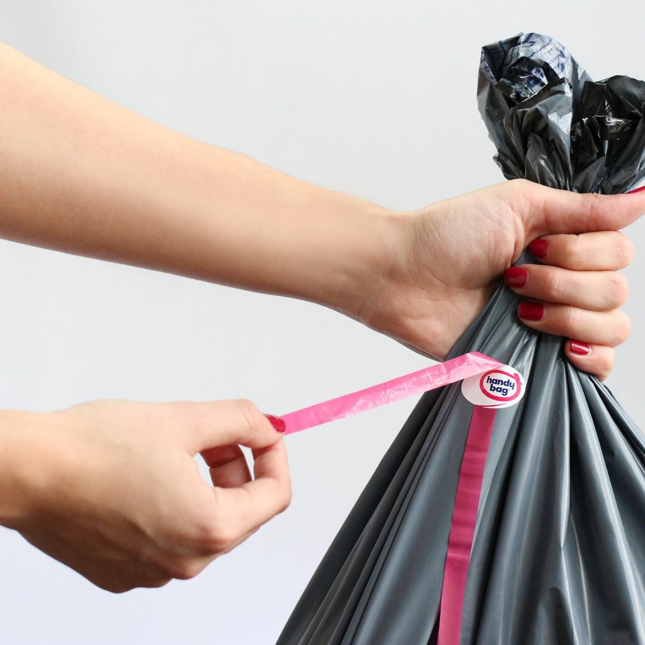 Main tirant le lien rose d’un sac poubelle gris Handy Bag sur fond clair