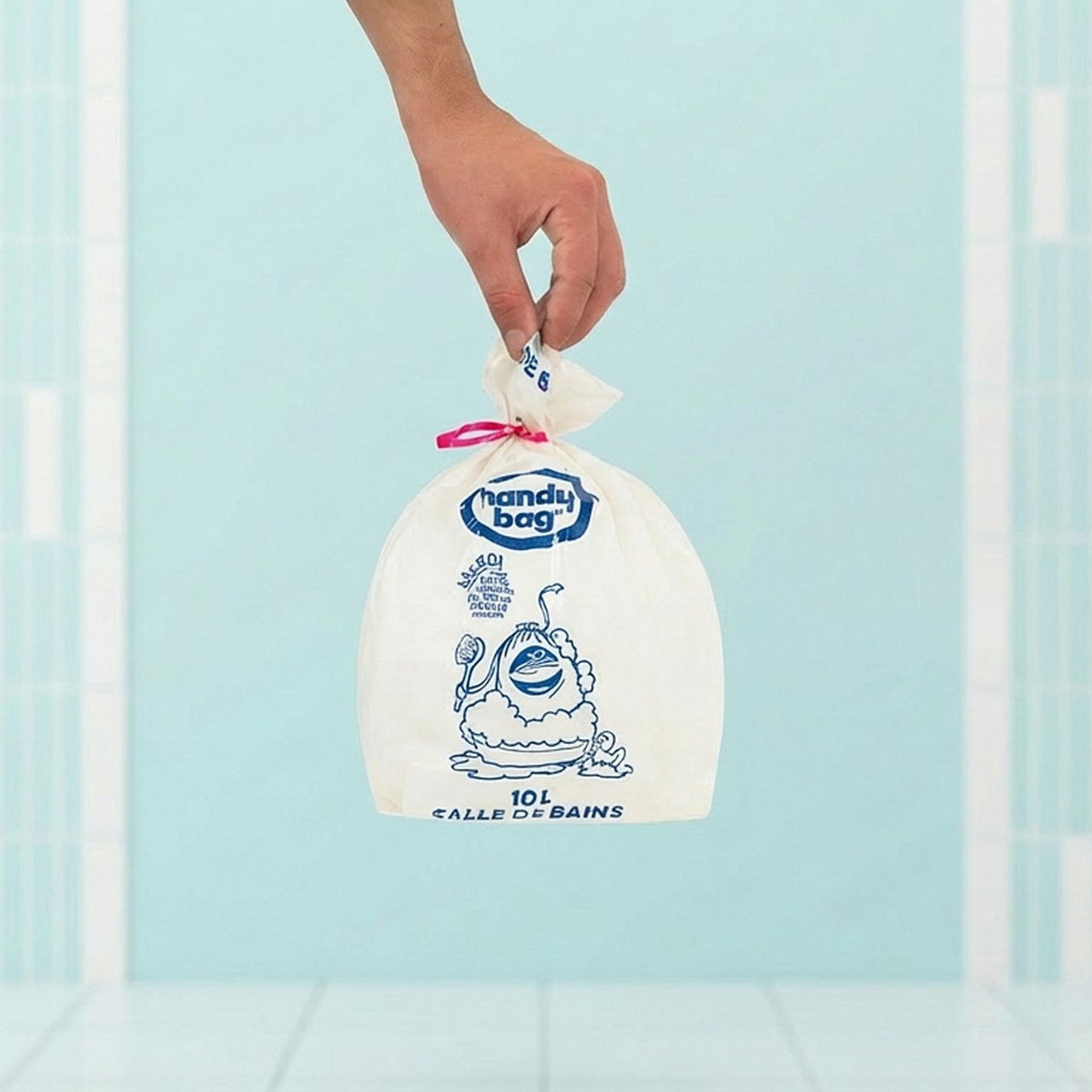 Main tenant un sac Handy Bag salle de bains sur fond bleu clair