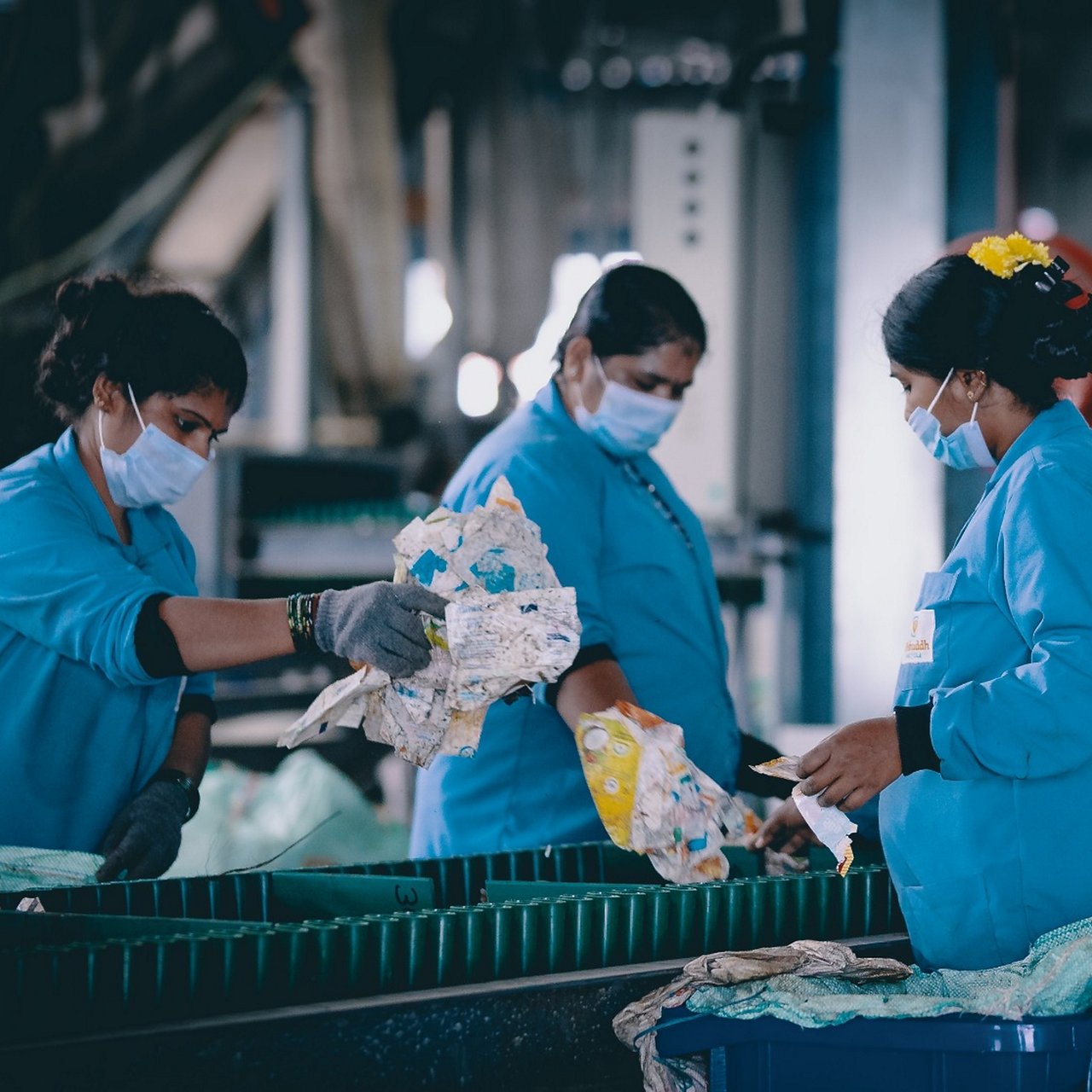 Travailleuses masquées triant des déchets sur une chaîne dans une usine de recyclage