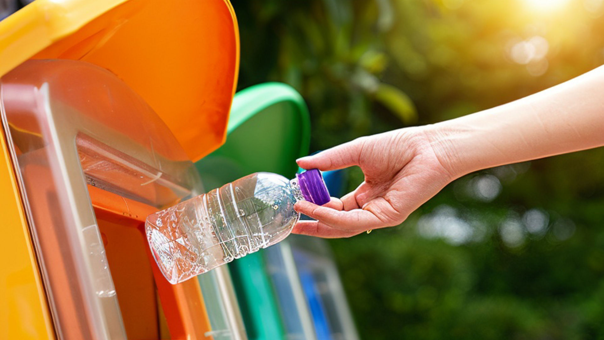 Main déposant une bouteille en plastique dans une poubelle de tri sélectif