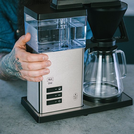 Melitta® One Filter Coffee Maker 6780184 front view from the top coffee machine placed on kitchen table water tank filled with water hand holding the coffee machine