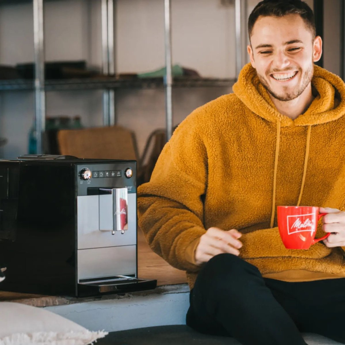 Melitta® Kaffeevollautomat Melitta Purista Schwarz-Silber 6769697 70 – Man enjoying coffee while machine brews in background, cozy lifestyle setting