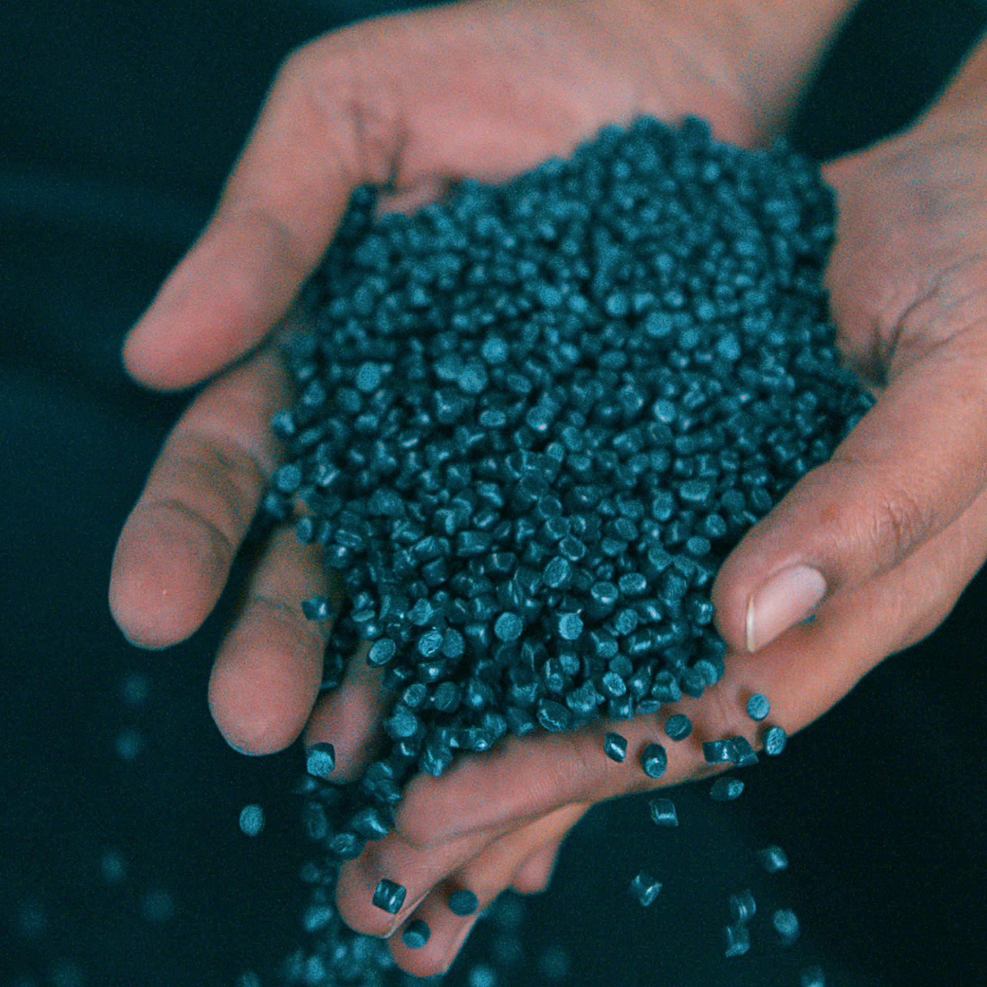 Recyceltes Plastikgranulat rinnt durch offene Hände