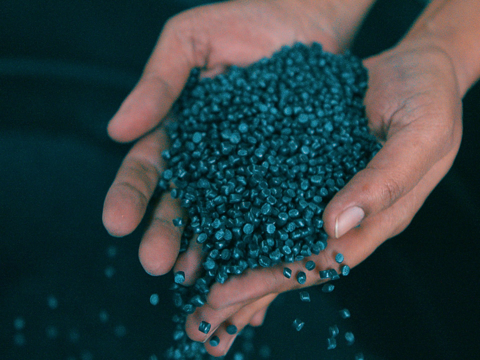 Recyceltes Plastikgranulat rinnt durch offene Hände