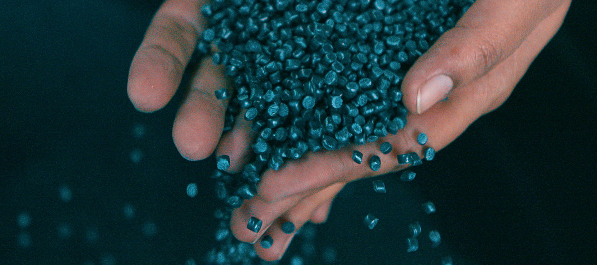 Recyceltes Plastikgranulat rinnt durch offene Hände