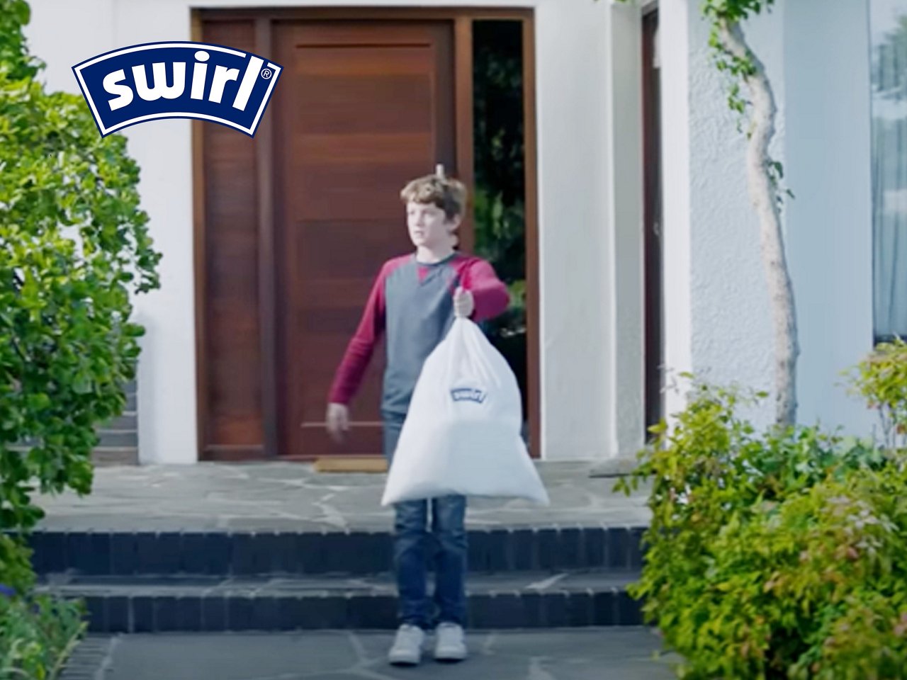 Junge steht draußen vor Haustür mit Swirl Müllbeutel in der Hand