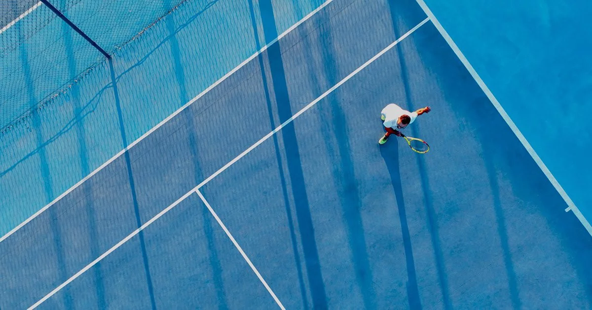 Directly above view of a tennis player on a blue tennis court.