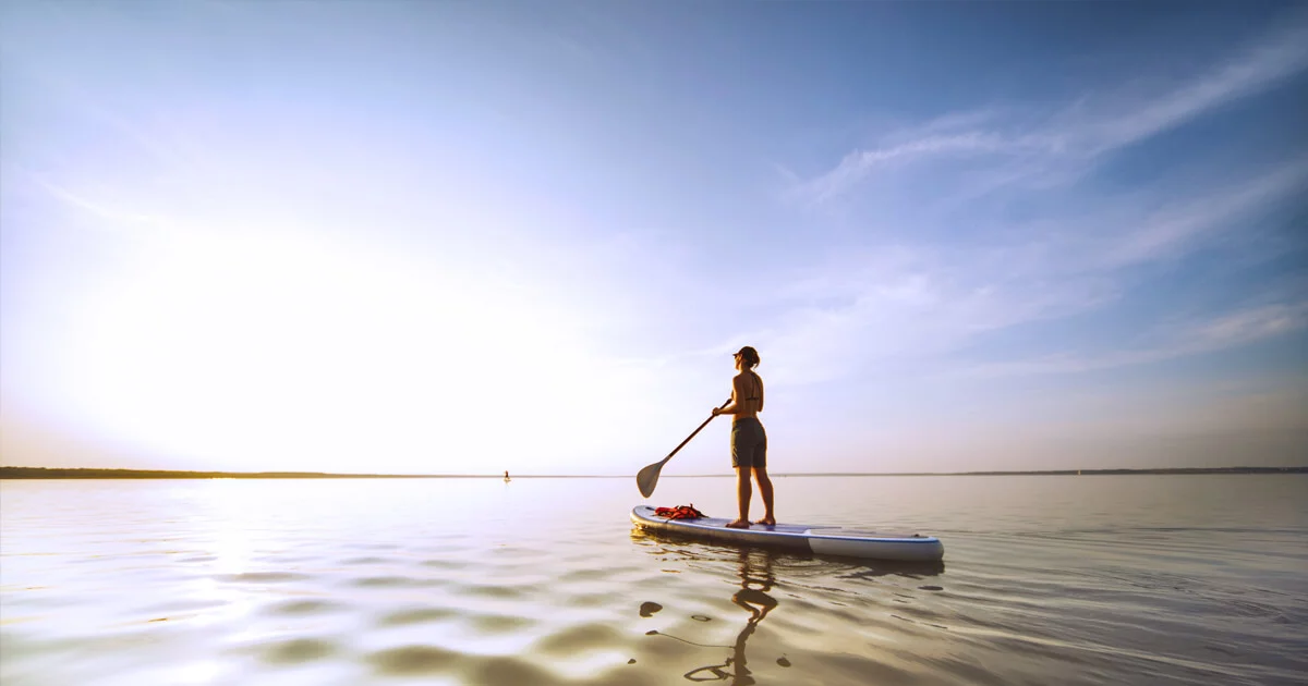 Woman balancing on a canoe in water and facing towards the sky.