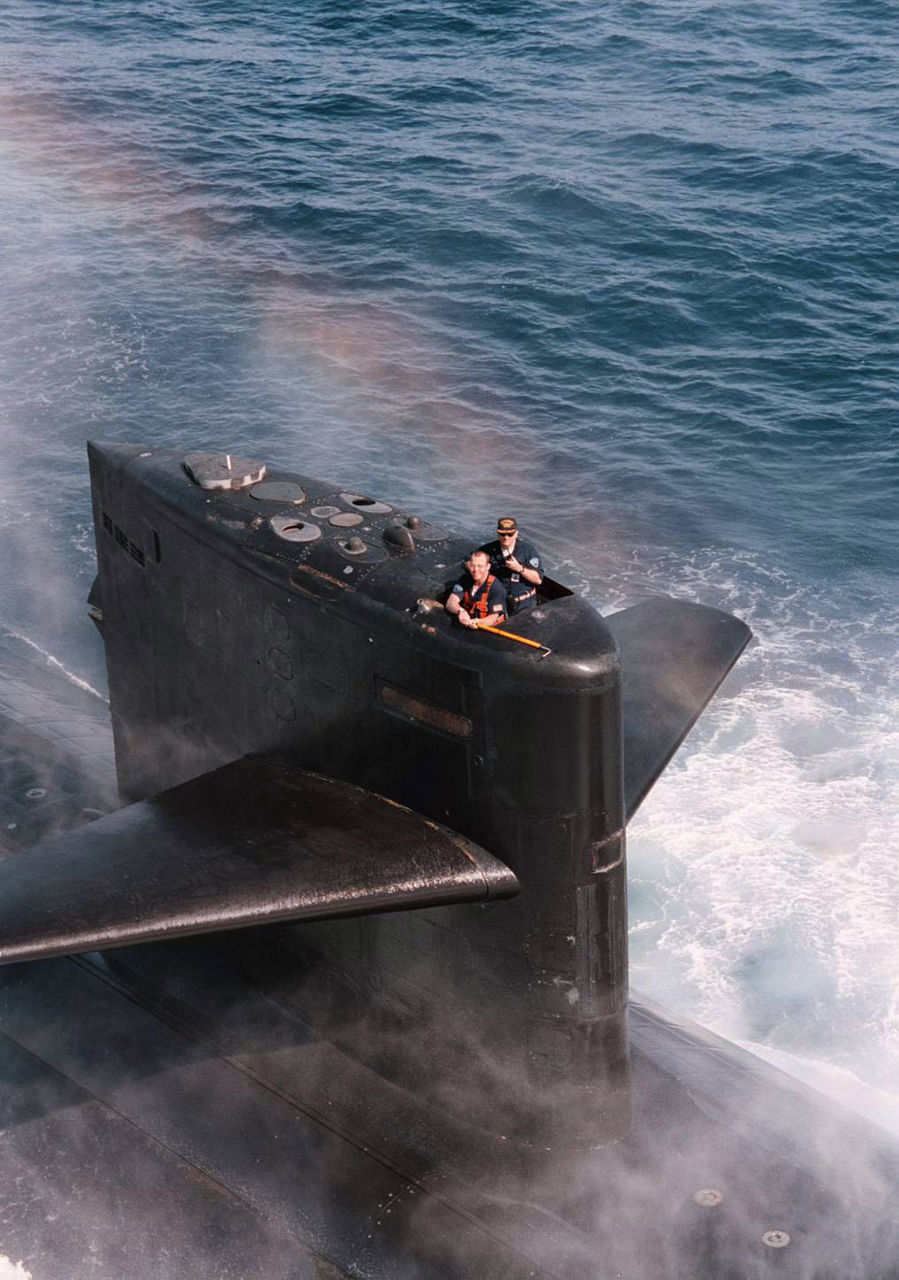 A rainbow arcs above a surfaced submarine as two crew members emerge.
