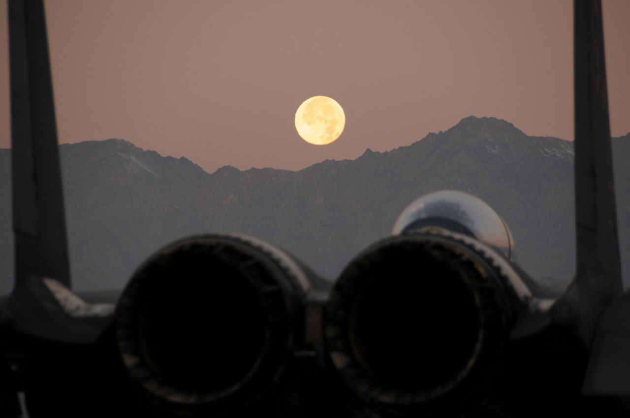 A full moon shines above the hills outside Bagram Air Field, Afghanistan, with a fighter jet in the foreground. (Photo credit: MSgt Joseph Harwood, Ohio Air National Guard)