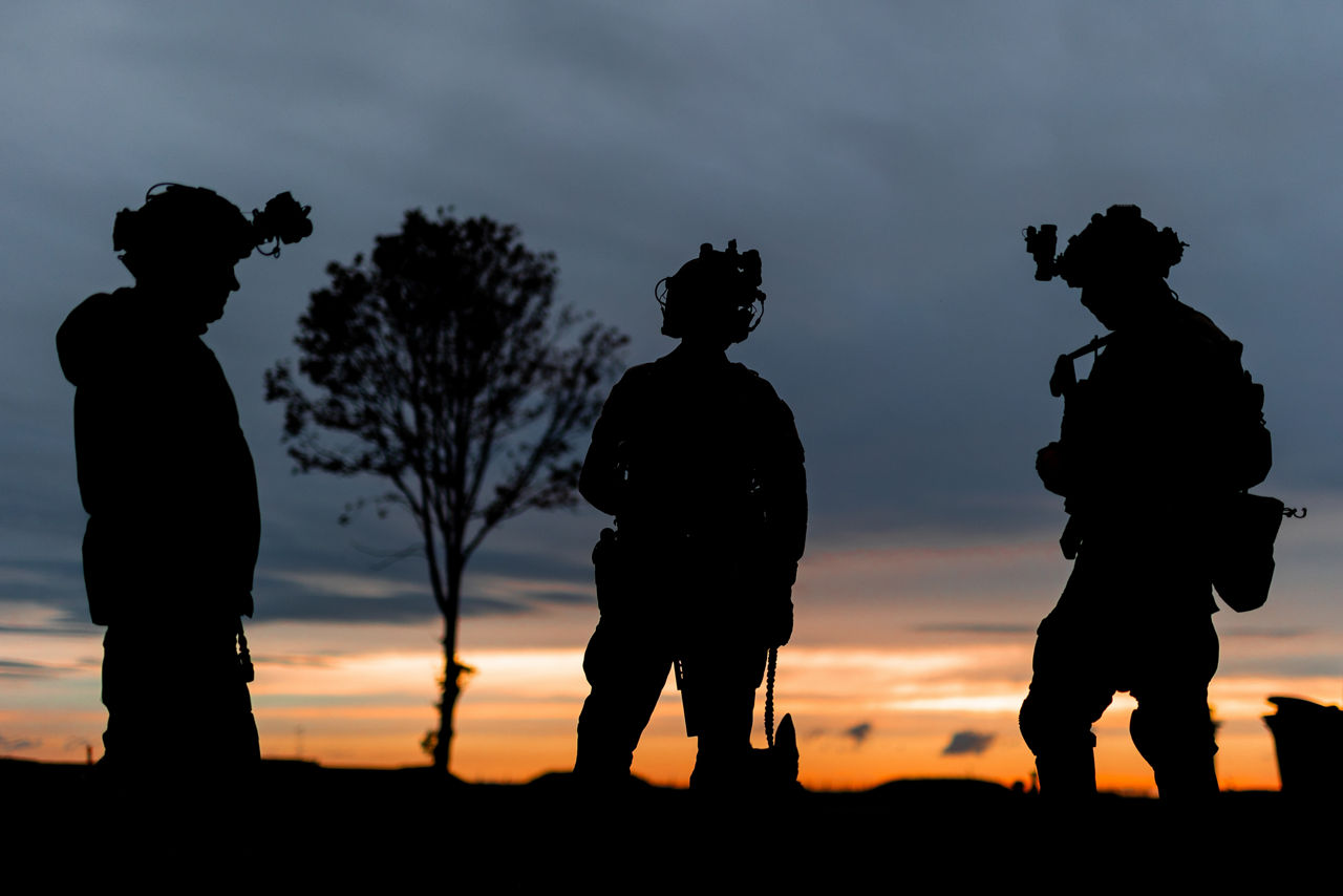 Three special forces operators (and their dog) huddle together at sunset during exercise Night Hawk 21 in Denmark.