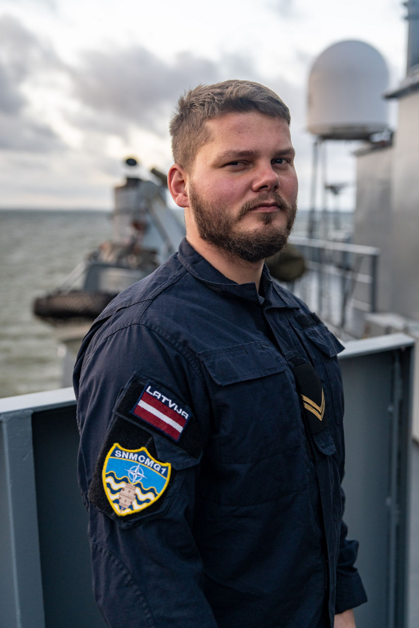 A Latvian sailor aboard SNMCMG1’s flagship LVNS Virsaitis poses for a portrait while the ship sails during exercise Freezing Winds.

NATO and its Allies are intensifying efforts to protect vital sea routes and critical infrastructure. Exercise Freezing Winds 2025 brought together ships from Standing NATO Mine Countermeasures Group One (SNMCMG1) and other Allied units to train side by side in the Baltic Sea’s harsh winter conditions. Over several days, naval forces, divers, and mine counter-measure teams practised joint operations to ensure readiness against diverse threats — from detecting and neutralising underwater threats to responding to disruptions affecting vital sea lines of communication. This exercise complements NATO’s Baltic Sentry enhanced vigilance activity, launched in January 2025 to strengthen surveillance and monitoring across the region. The exercise took place from 24 November to 4 December 2025.