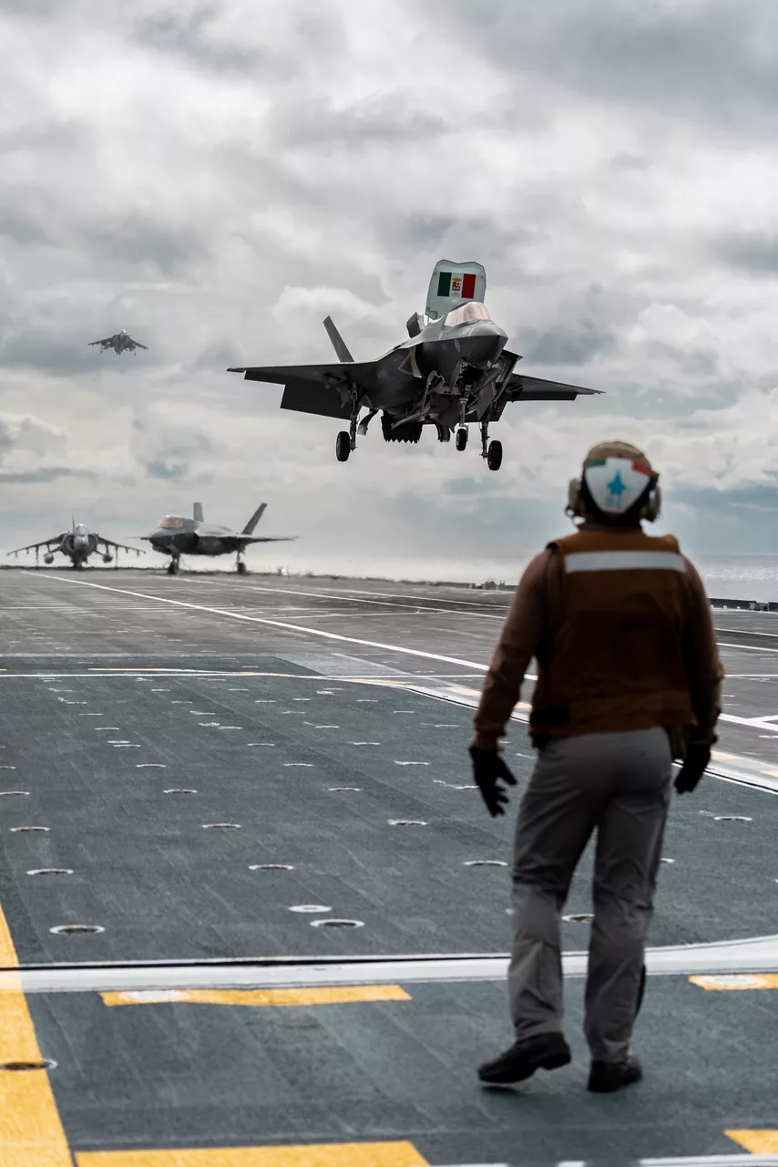 An Italian Navy sailor watches as an F-35B Lightning II fighter prepares to land aboard the aircraft carrier ITS Cavour, with an AV-8B Harrier II trailing behind during Neptune Strike, an enhanced Vigilance Activity taking place in the Western and Central Mediterranean Sea from 25 March to 1 April 2026. Naval Striking and Support Forces NATO (STRIKFORNATO), a Portugal-based maritime command, leads several Neptune Strike iterations every year, focusing on improving Allied integration at sea while expanding our presence and awareness. This iteration involved Carrier Strike Groups from France, Italy and Spain.