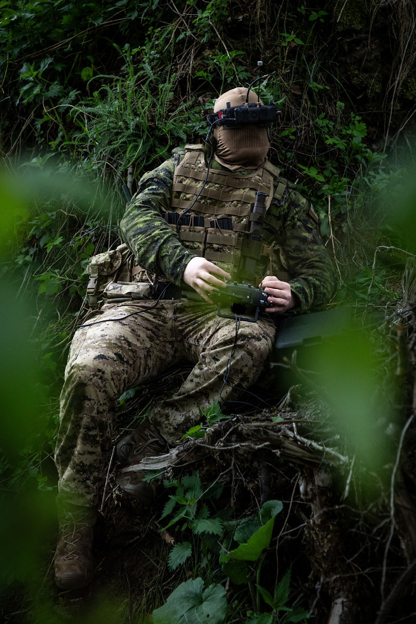 A Canadian Armed Forces drone pilot operating an FPV drone using goggles and hiding in nature. NATO’s Multinational Brigade in Latvia regularly runs training exercises where troops integrate drones of all kinds, making sure Allied forces keep pace with innovations in modern wafare.