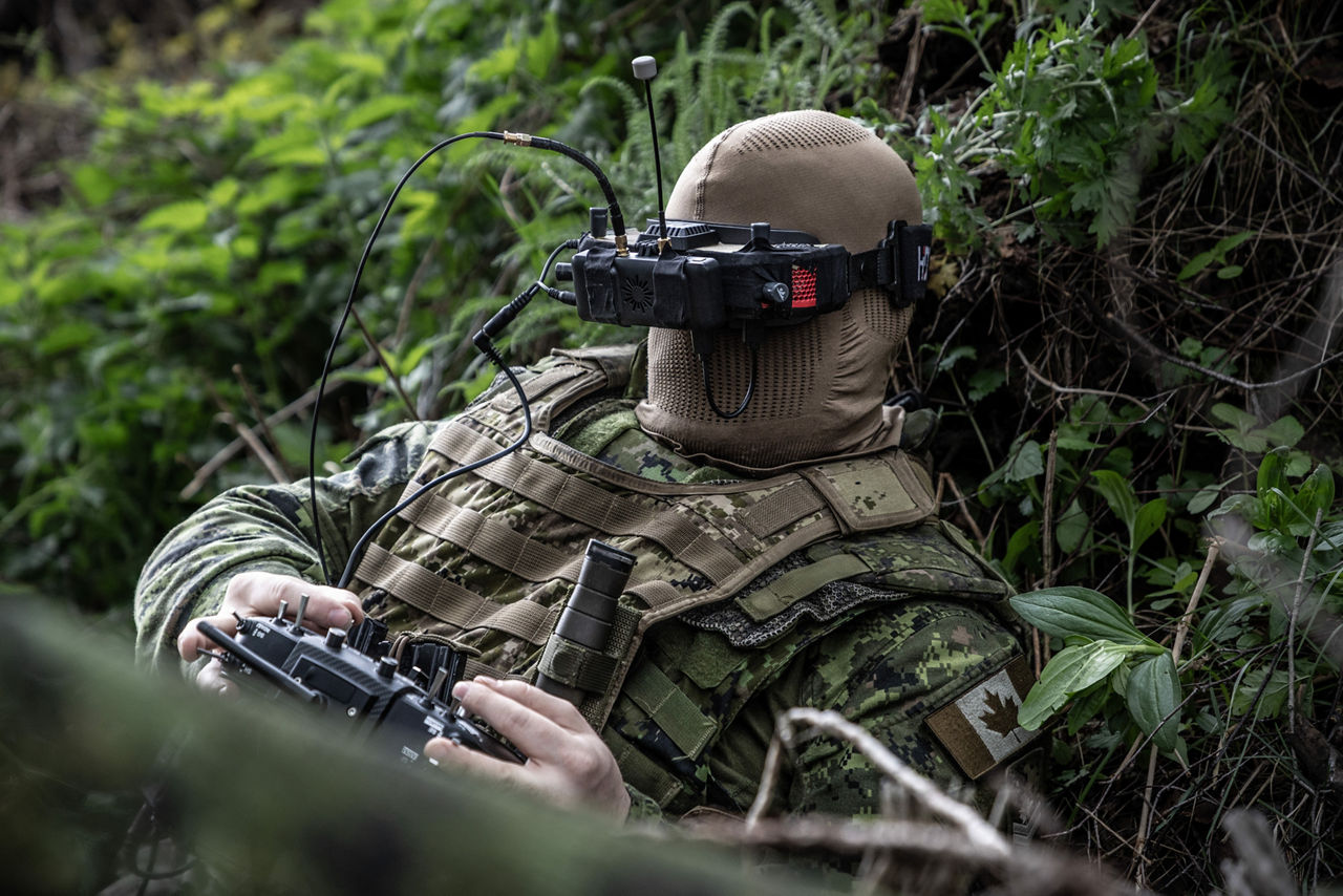 A Canadian Armed Forces drone pilot operating an FPV drone using goggles while hiding in nature. NATO’s Multinational Brigade in Latvia regularly runs training exercises where troops integrate all kinds of drones, making sure Allied forces keep up with innovations in modern warfare.