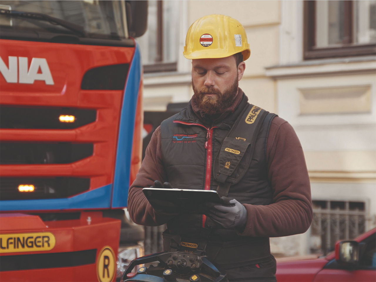 Un technicien de terrain portant un casque de sécurité et des gants utilise une tablette pour inspecter l’équipement monté sur un camion de service en plein air.