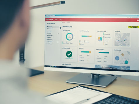 Fleet management dashboard displayed on a desktop monitor, showing analytics, service status, and vehicle overview in a modern office setting.
