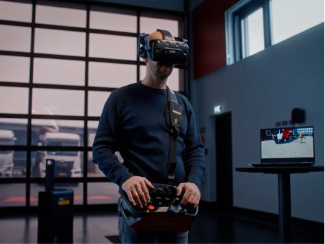 Operator using a virtual reality headset and handheld controller to simulate crane or vehicle operations inside a training environment.
