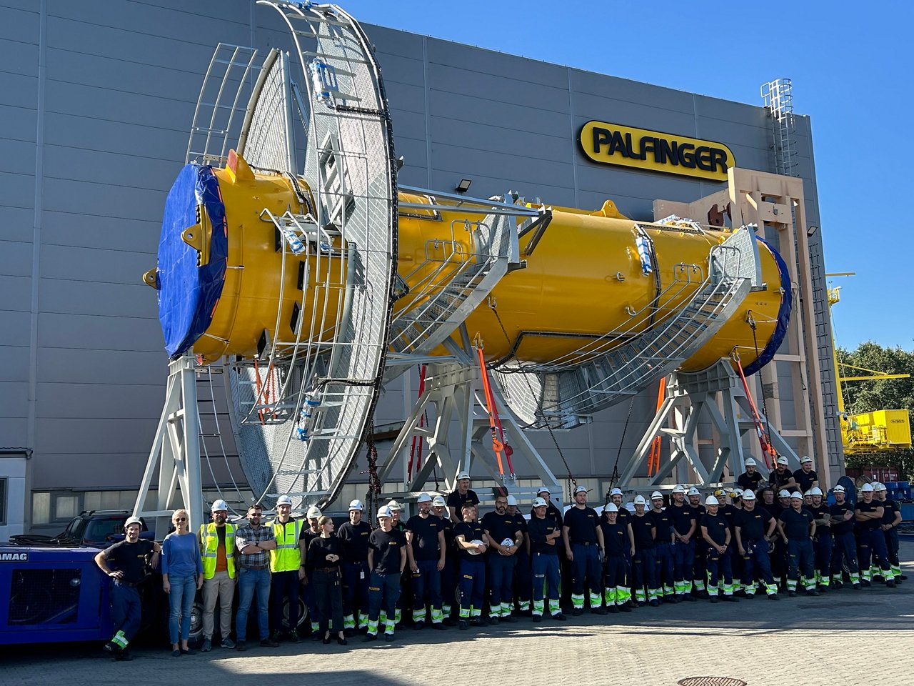 PALFINGER team posing outside the Gdynia facility in Poland in front of a jib crane pedestal