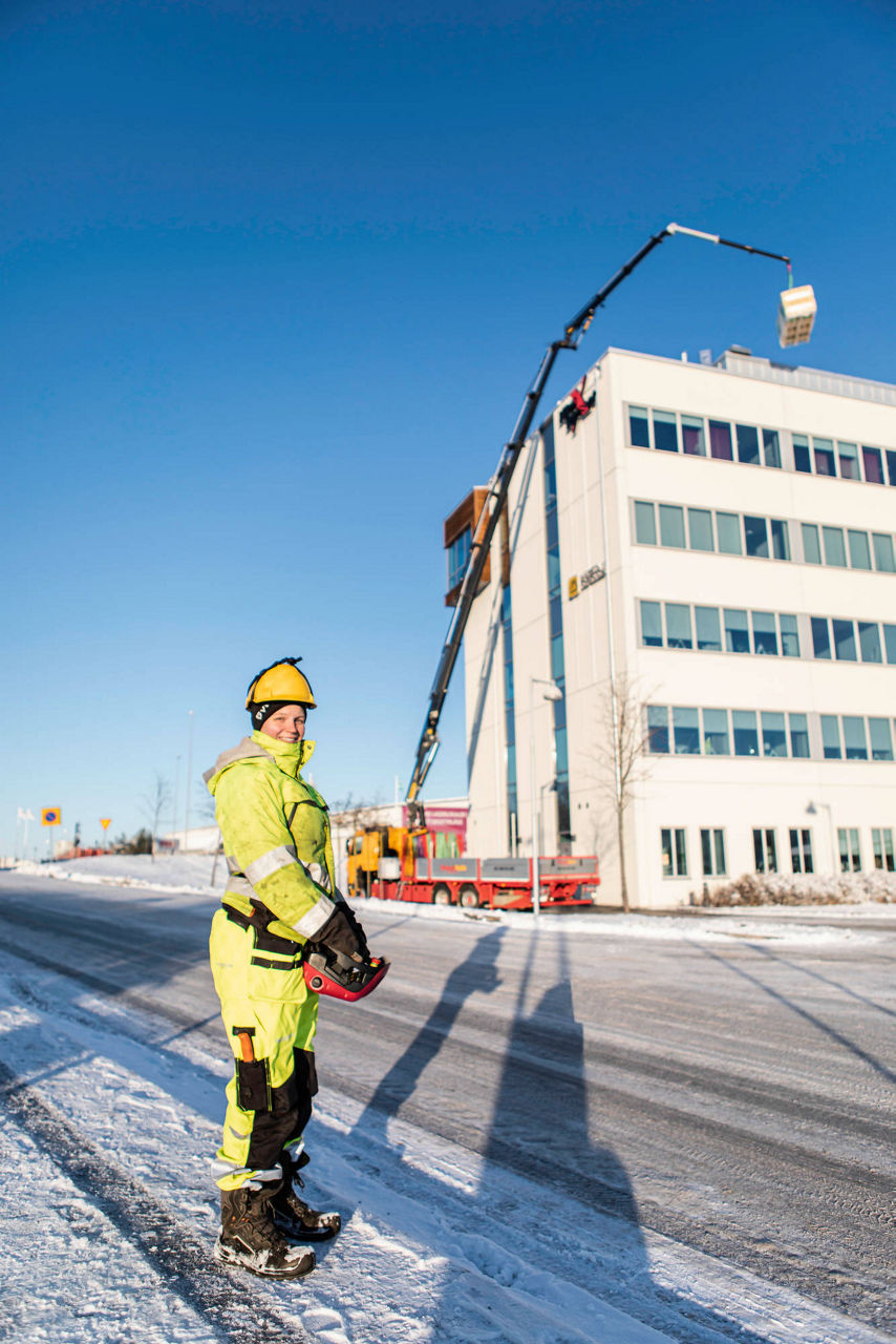 Worker in yellow safety gear operating a PALFINGER PK37002 loader crane mounted on a red vehicle in front of a modern building during winter conditions