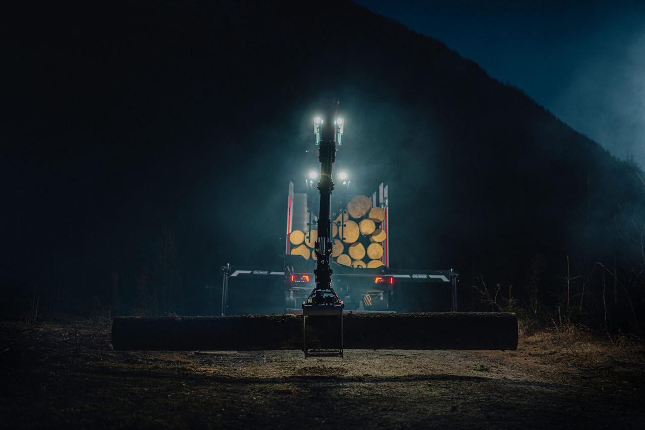 Palfinger Epsilon Kran bei Nacht, der einen Baumstamm hält, erhellt von den die LED-Kranleuchten