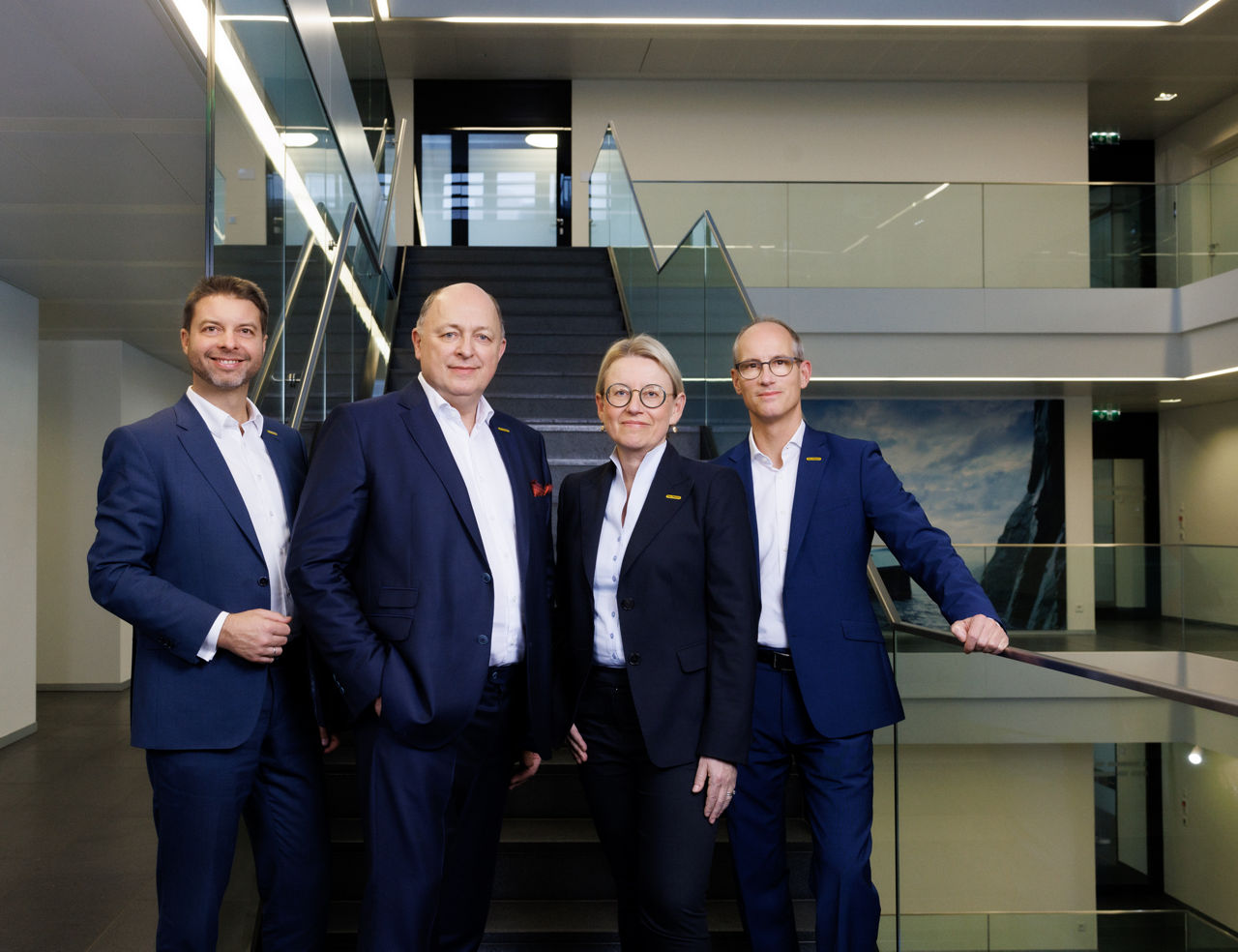 A group of professionally dressed individuals standing in a modern office building, symbolizing leadership and teamwork.