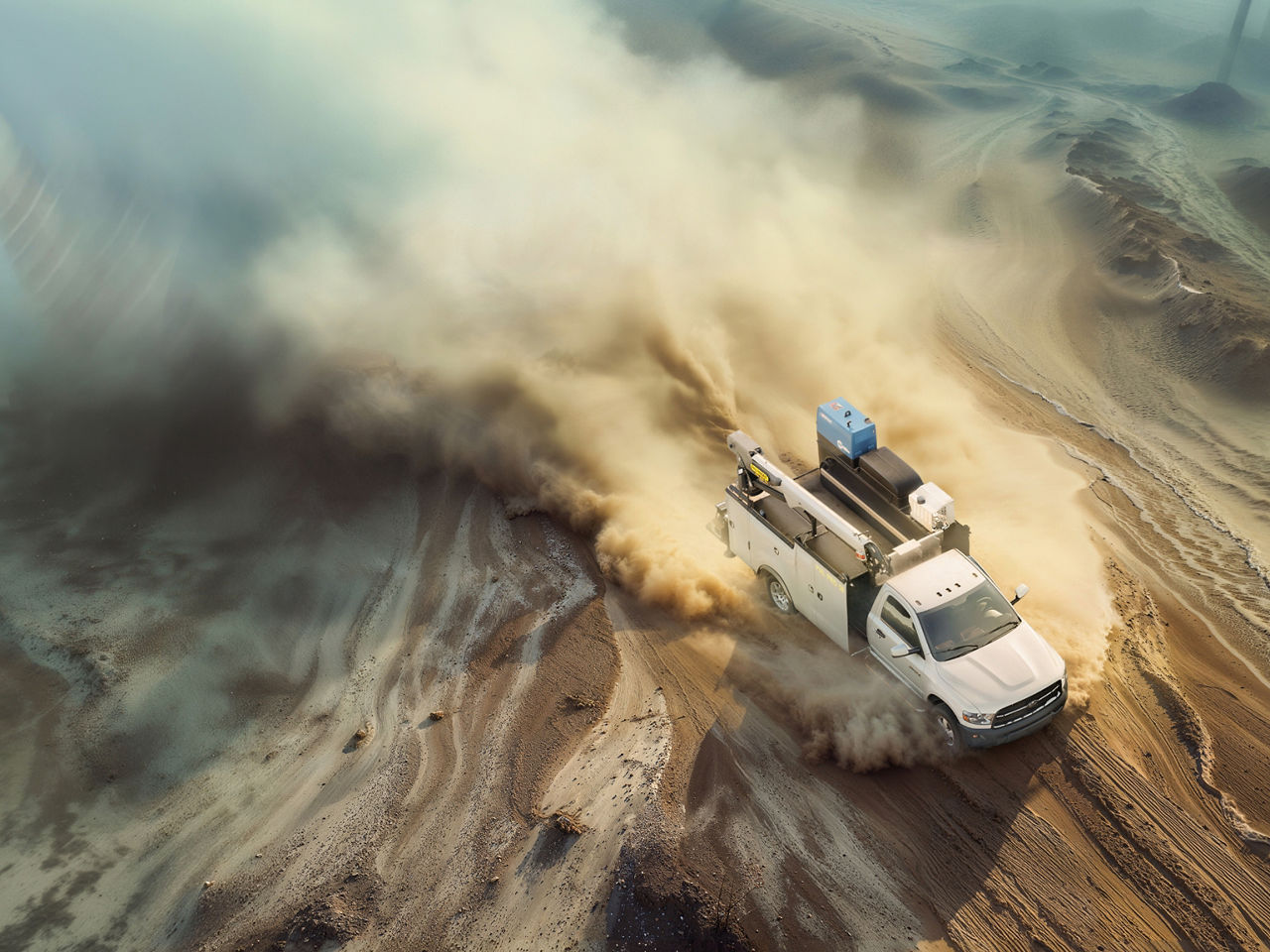 Aerial view of a service vehicle driving through a dusty landscape, shown from a neutral top-down angle.