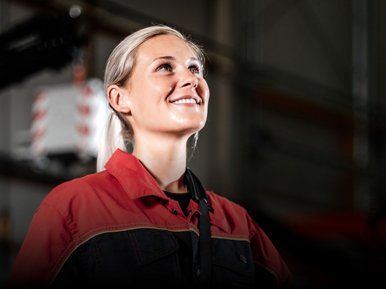 Portrait of a smiling worker in red workwear, softly lit with a subtle dark gradient in the background.