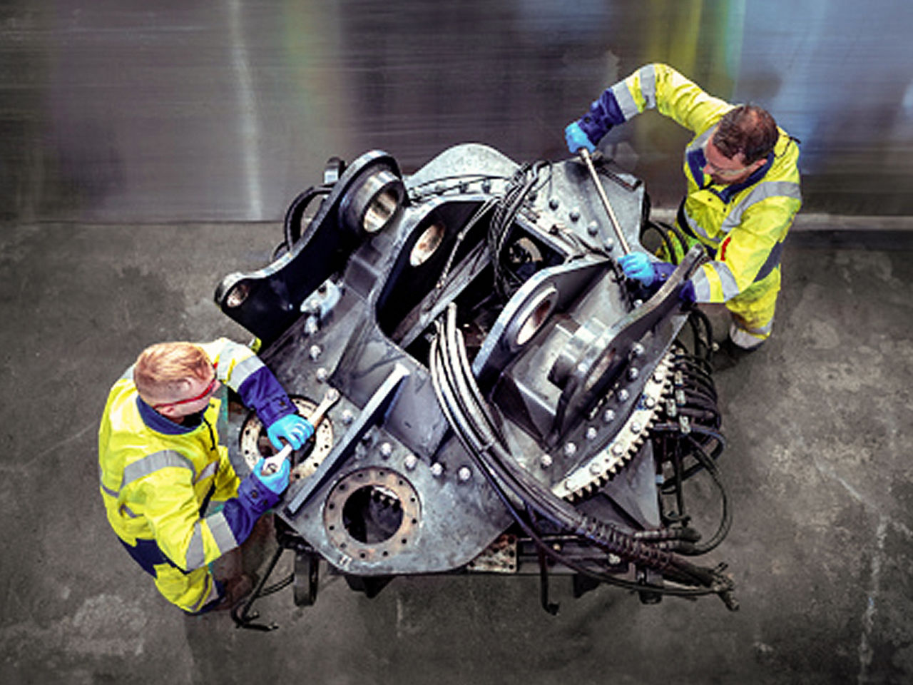 Two technicians in high-visibility clothing working on machinery indoors, shown with natural, balanced colors.