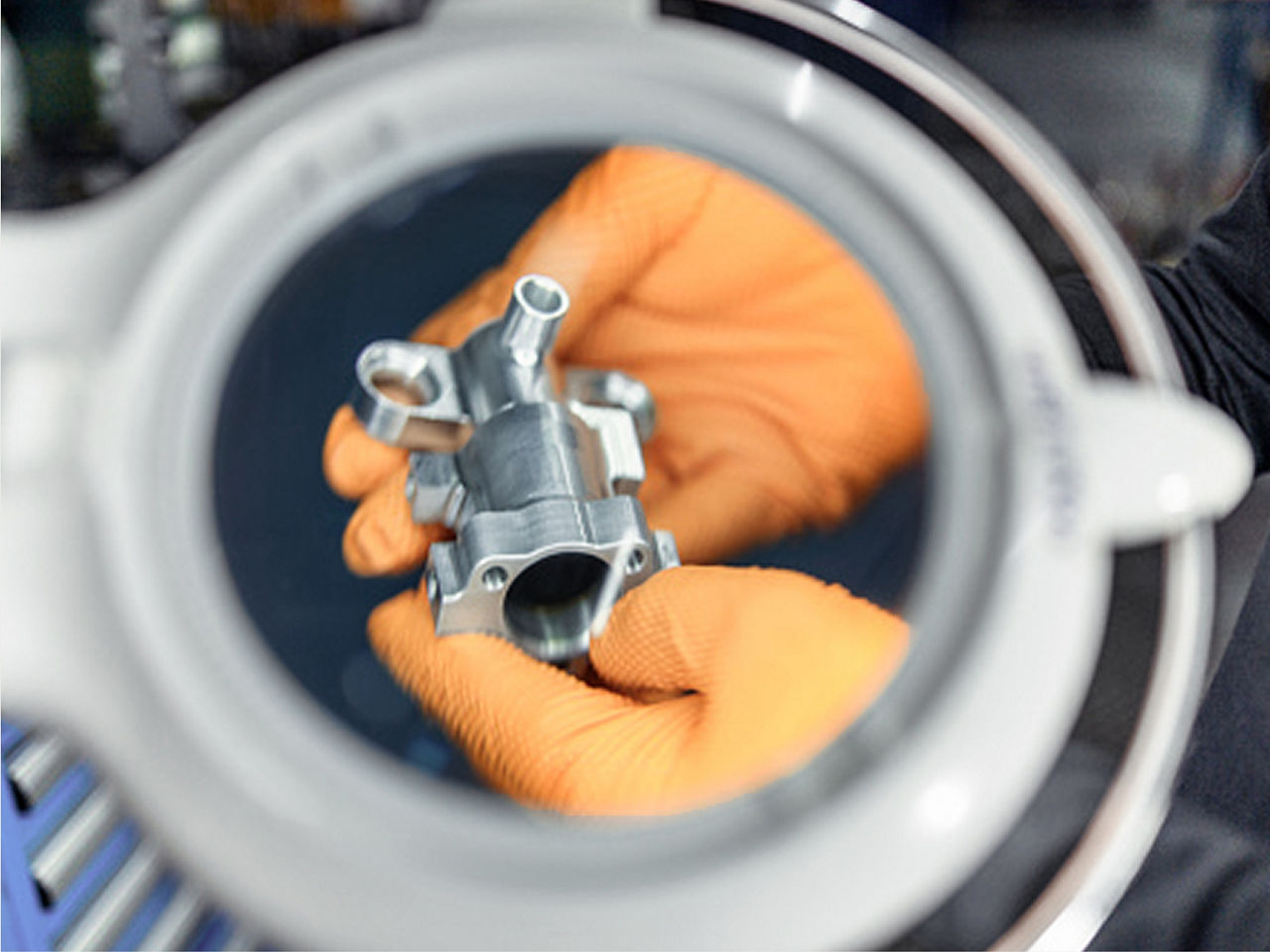 Close-up of gloved hands holding a metal component, sharply focused against a softly blurred background.