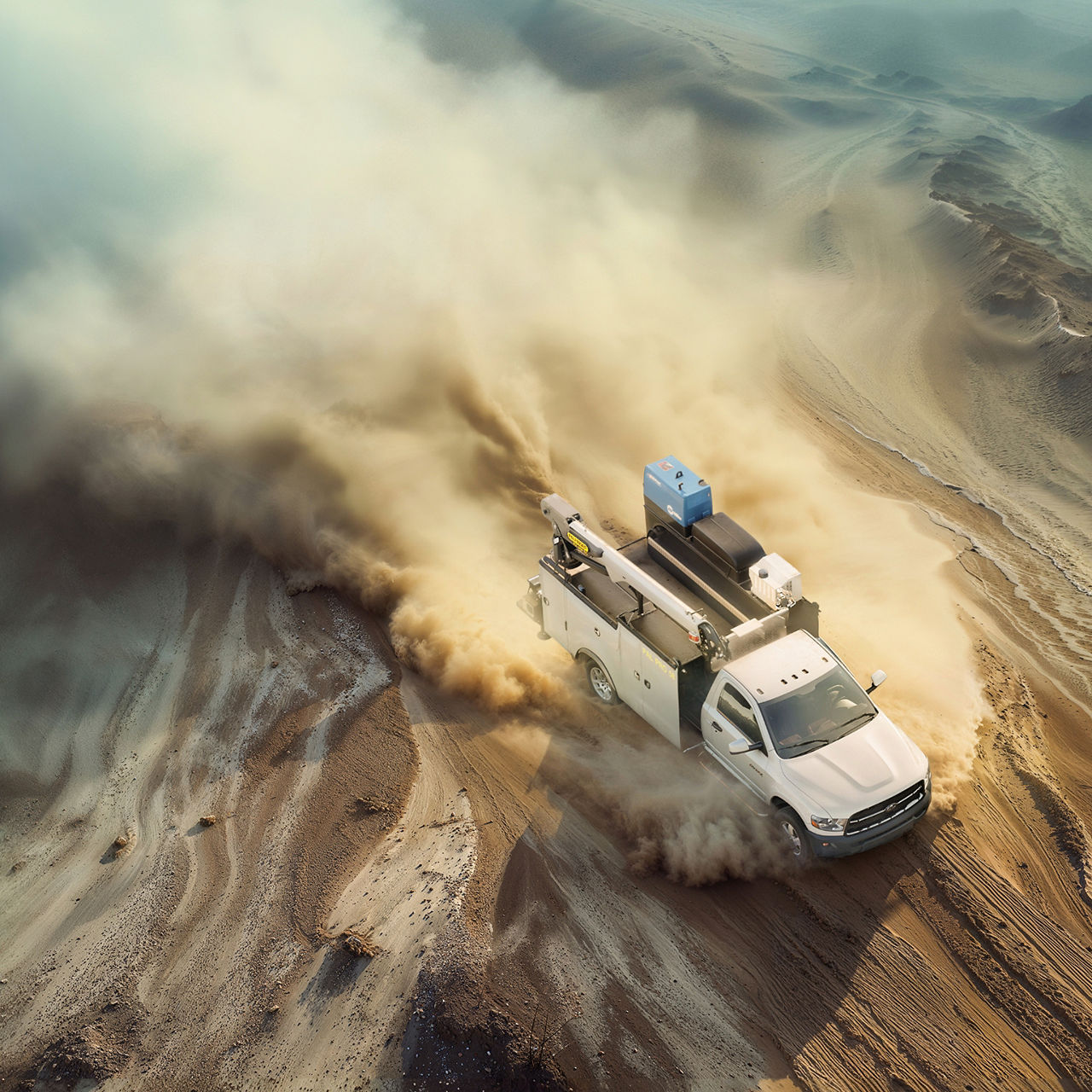 Ein Service-LKW fährt durch eine sandige Wüstenlandschaft und wirbelt beim Fahren über unwegsames Gelände Staub auf.