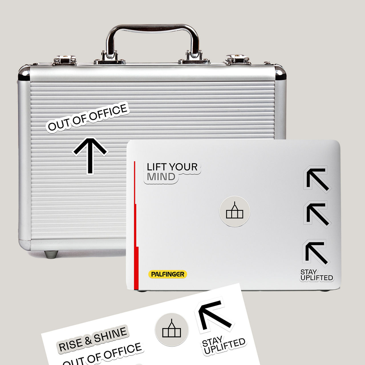 Silberne Aktentasche und weiße Laptoptasche, gestaltet mit PALFINGER-Branding, Pfeilsymbolen und Aufklebern mit den Aufschriften OUT OF OFFICE, LIFT YOUR MIND, RISE & SHINE und STAY UPLIFTED, angeordnet als Lifestyle-Markenkomposition.