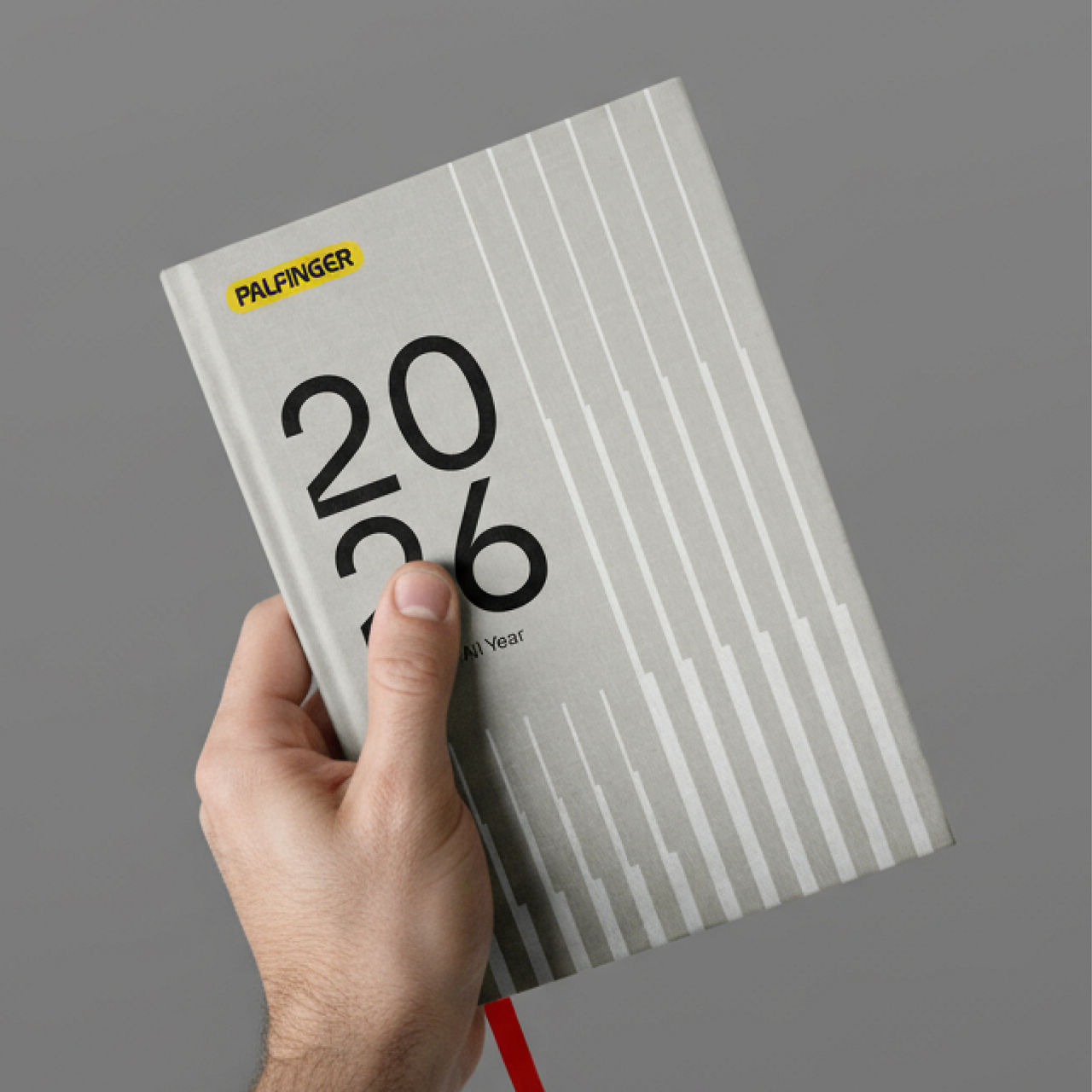Hand holding a grey PALFINGER notebook with large “2026” typography and a subtle vertical line pattern on the cover.