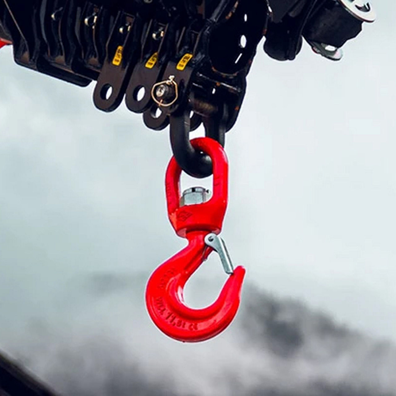 Nahaufnahme eines roten Hubhakens, der an einem schwarzen Ladekranmechanismus vor einem weichen, neutralen Hintergrund befestigt ist.
