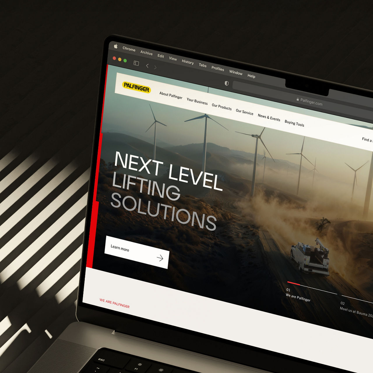 Ein Laptop, auf dem die Website von PALFINGER angezeigt wird, wobei die Uplifting Line als vertikales rotes Markenelement erscheint und das digitale Layout einrahmt.