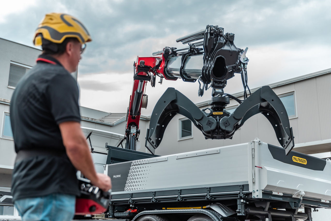 Worker operating a Palfinger loader crane with hydraulic grapple on a truck.
