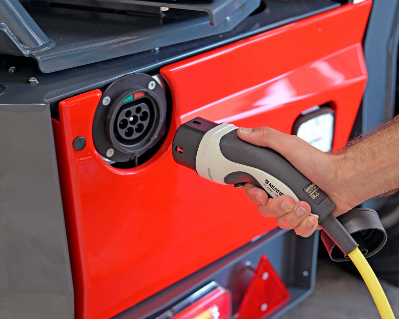 A hand plugging a charging connector into the Palfinger FLS25 electric truck-mounted forklift charging port.