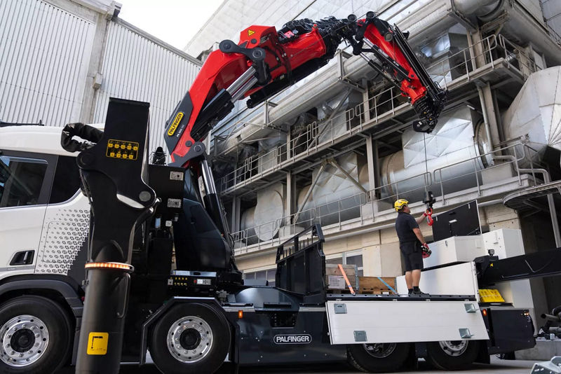 Montagem industrial com braço robótico instalado em caminhão guindaste, técnico trabalhando na área de máquinas e estruturas metálicas em ambiente fabril.