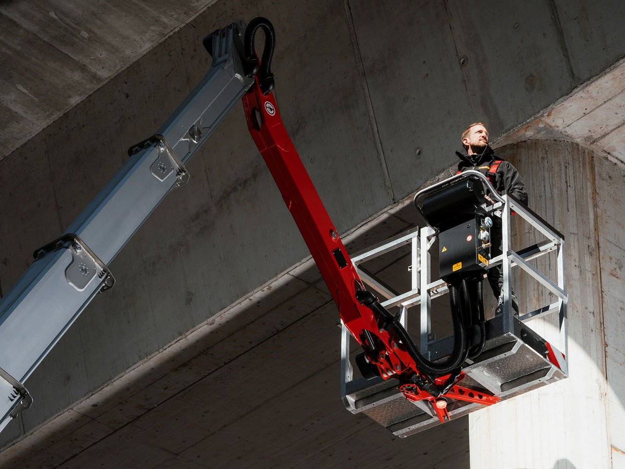 Operator standing in an elevated work platform, using a PALFINGER lift beneath a concrete structure.