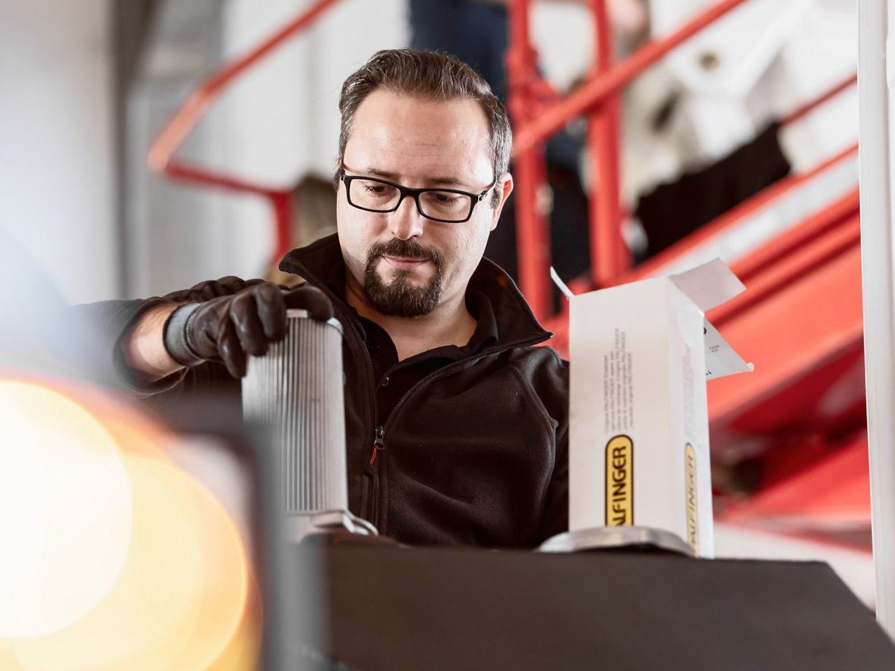 Technician inspecting a PALFINGER component by hand in a workshop environment, focused on precise handling.