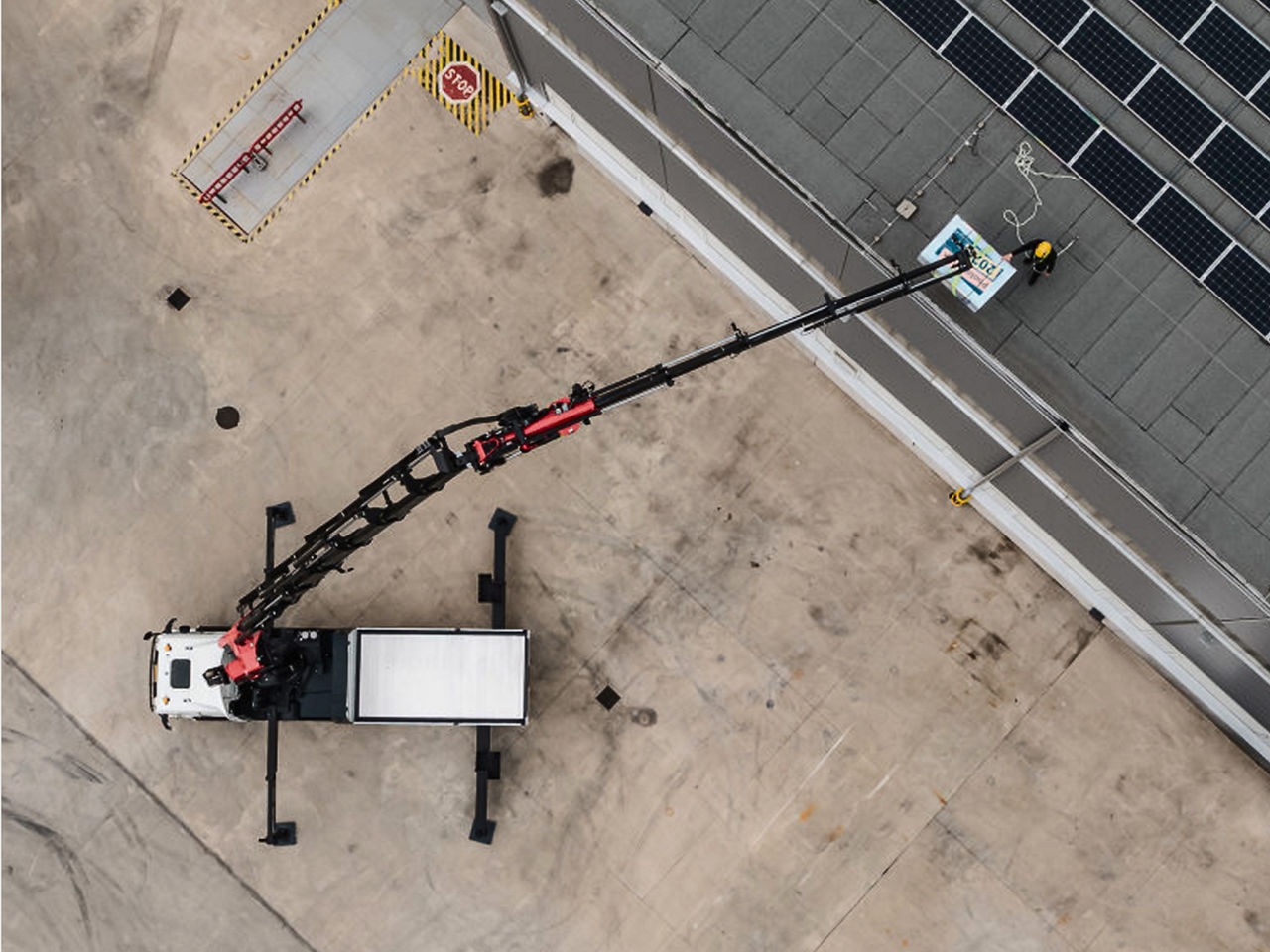 Top-down view of a truck-mounted crane and lifting platform extended over a rooftop, presenting the full system layout with clear, factual detail.