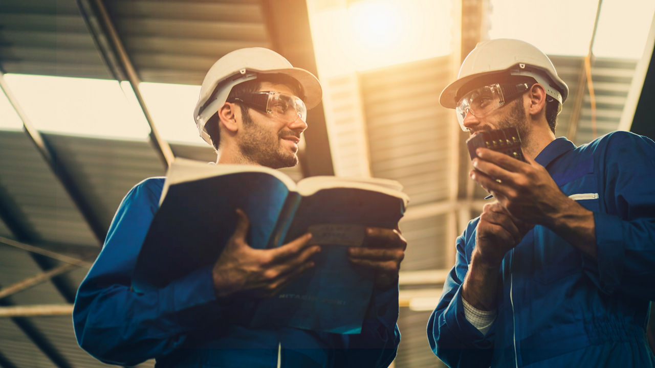 The Industrial workers discuss the spare parts of the machine in factory with a manual guide book, the procedure of work in the factory, concept industrial workers process, manufacturing operation.