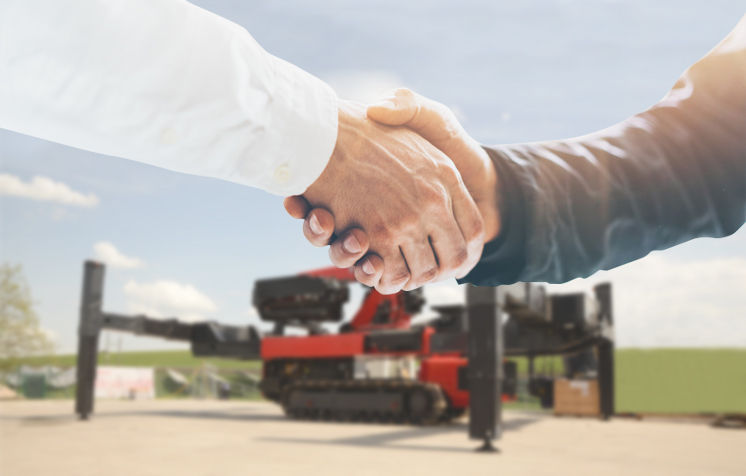 Two people shaking hands in front of a red PALFINGER crane setup on stabilizers, symbolizing partnership and a successful equipment deal.