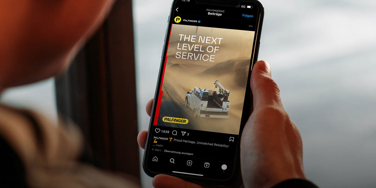 A person holding a smartphone displaying a branded social media post that reads “The Next Level of Service,” featuring industrial equipment imagery, conveying a modern, digital presentation of an industrial services brand.