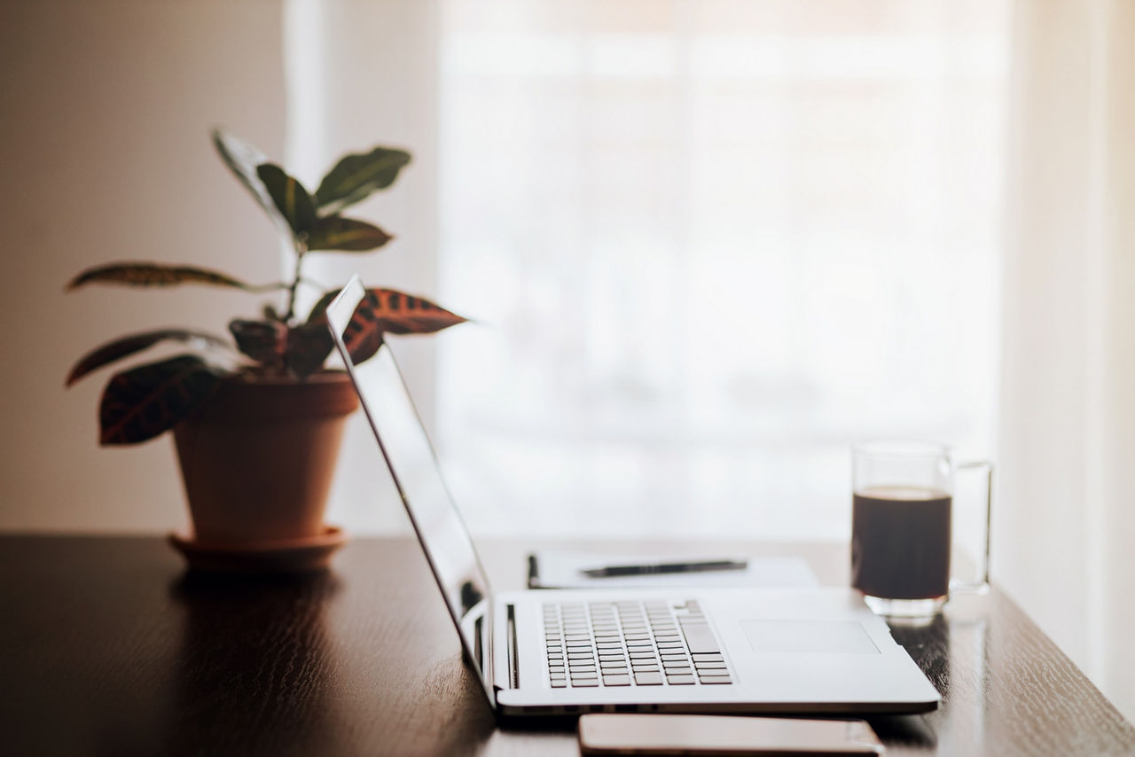 Workplace with laptop and phone at home. Laptop on wooden table with plant and coffee cup background. Work from home.