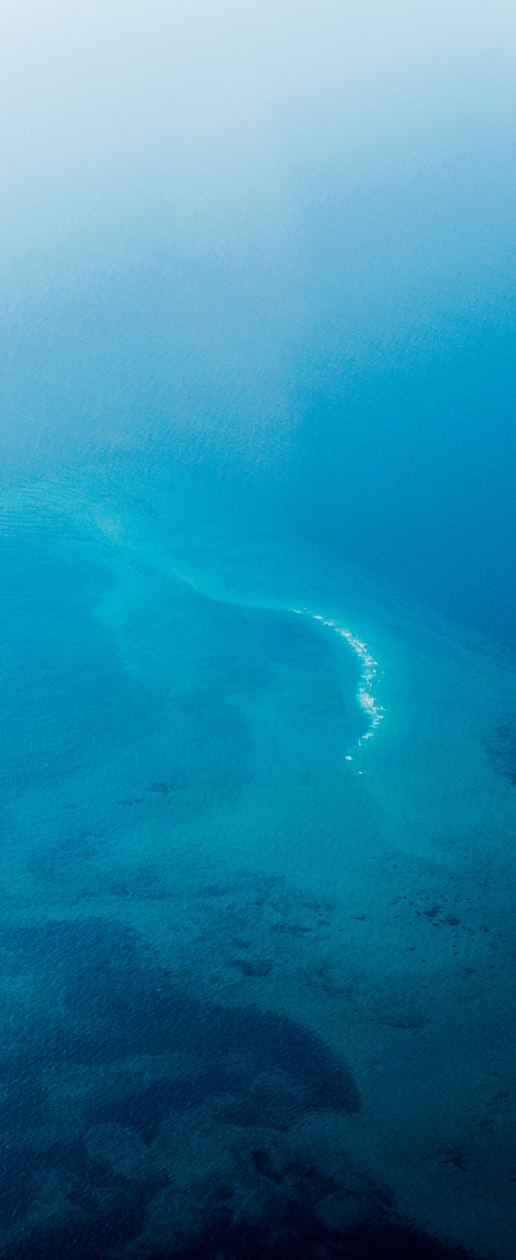 An aerial view of sea currents and a reef in the open ocean.