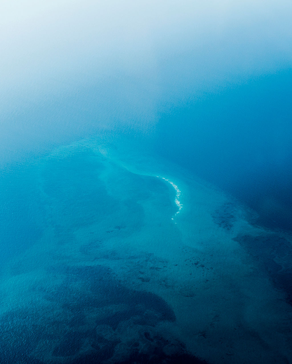 An aerial view of sea currents and a reef in the open ocean.