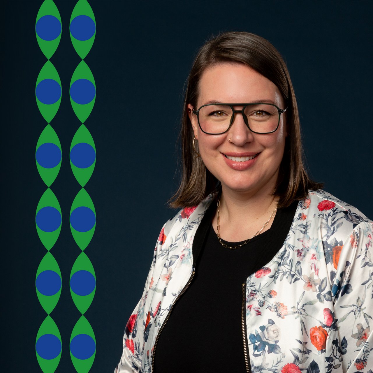 Jasmine Presson, Chief Strategy Officer bei Mediaplus North America. Porträt einer Frau mit Brille und schulterlangem braunen Haar, lächelnd vor dunkelblauem Hintergrund. Sie trägt eine florale Jacke über einem schwarzen Oberteil. Links im Bild verlaufen grafische grün-blaue Muster in vertikaler Linie.