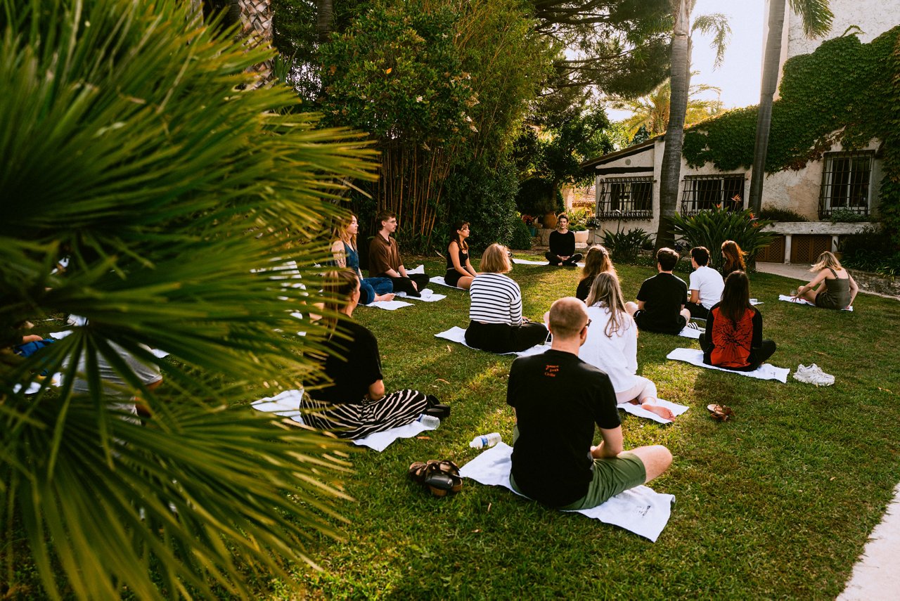 Spark Academy 2025 in Cannes: Gruppe von Teilnehmenden sitzt im Freien auf Handtüchern im Gras und meditiert gemeinsam unter Palmen im Garten einer Villa.